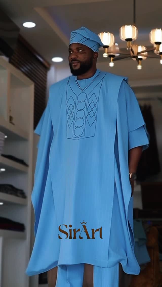 Man in a sky-blue agbada and matching cap standing in the SirArt showroom