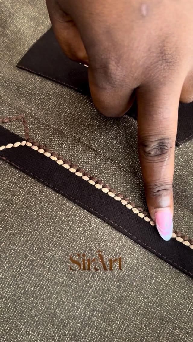 Fingertip tracing a line of hand-stitched beads along brown fabric