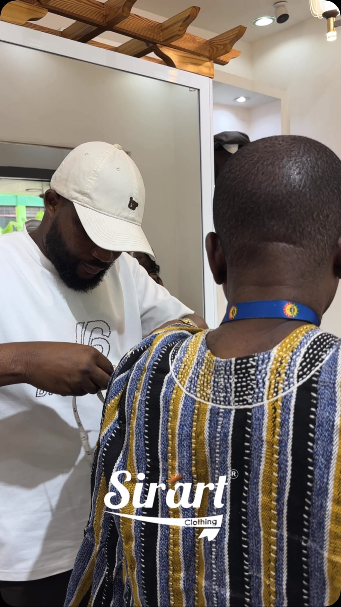 SirArt tailor adjusting a handwoven kente robe across a client’s shoulders