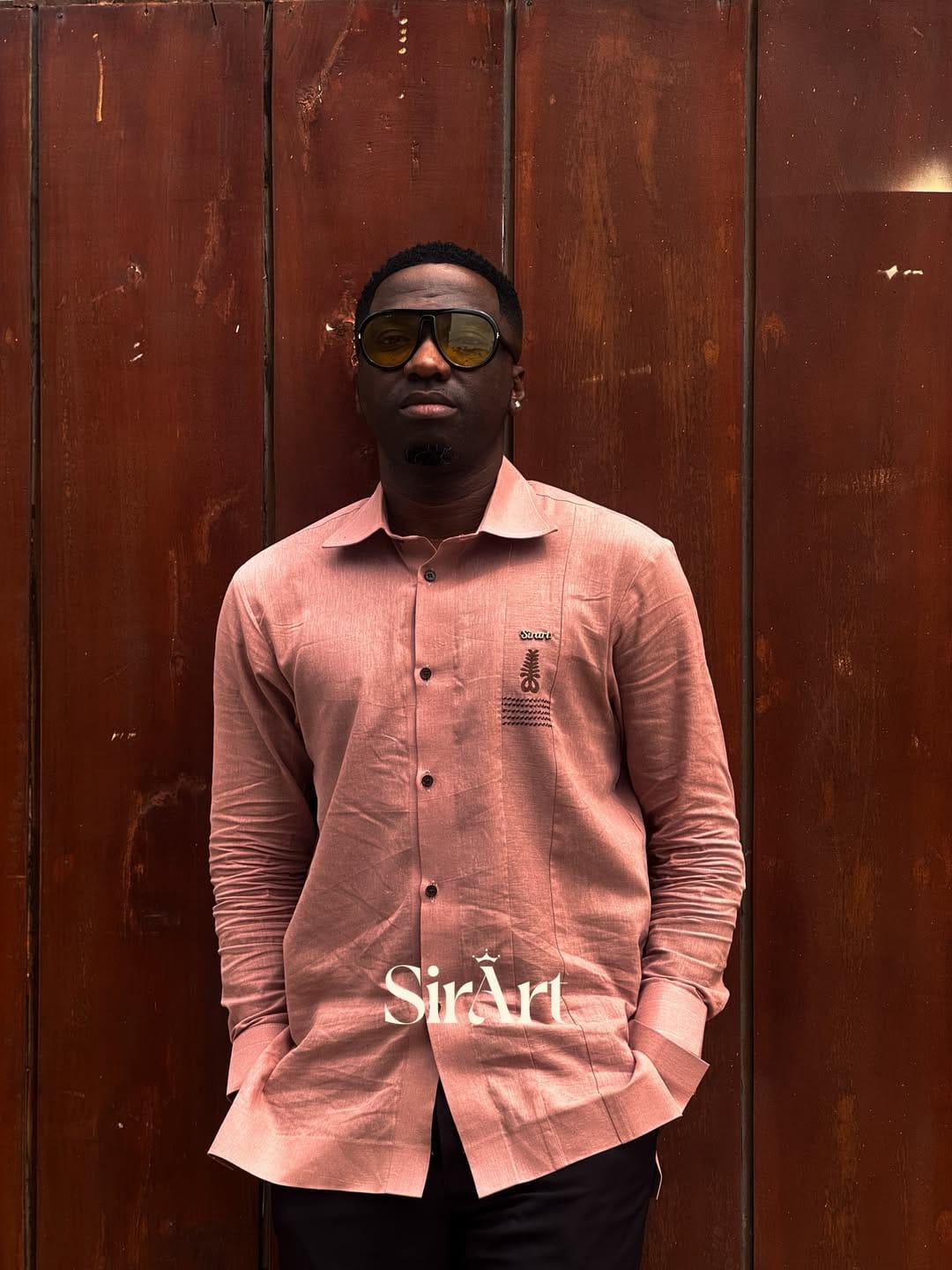 Man in a salmon linen SirArt shirt and sunglasses against a weathered wooden door